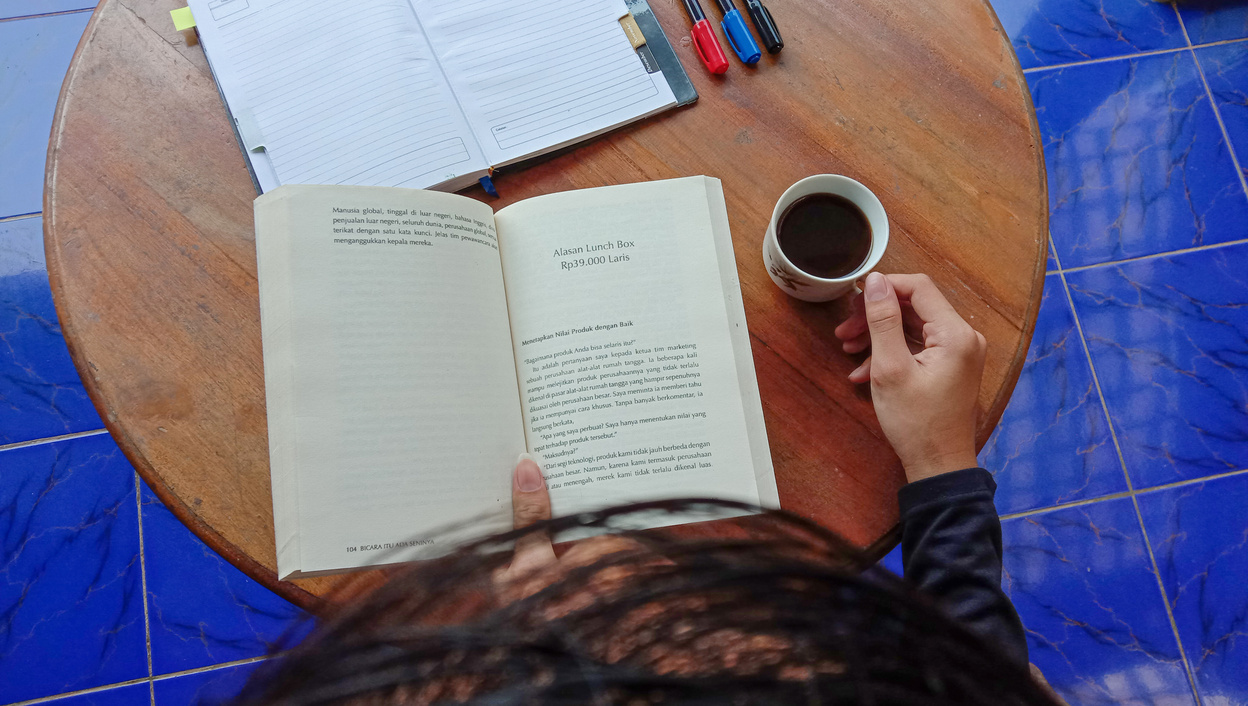 Person Reading a Novel Drinking a Cup of Coffee